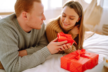 Couple in love on the bed spending time together. Man and woman relax and enjoy in bed at home. Concept of holiday, love, gifts.