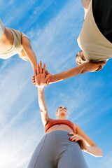 Low angle view of young group of sportive friends in circle stacking hands motivating each other before workout exercise routine in the street. Fitness, sport and teamwork concept. Vertical photo.