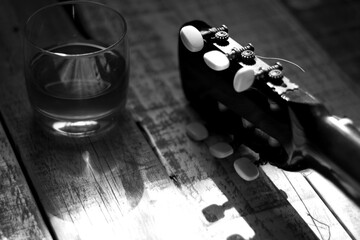 acoustic guitar headstock next to a glass of alcohol on aged white wood, concept of loneliness,...