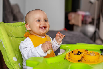 Baby sitting in high chair, eating puree or porridge. Baby eats complementary foods