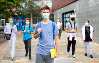Young student in a protective mask going to college down the city street