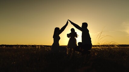 Silhouettes of parents against sky over daughter holding hands with setting sun. Figures of parents...