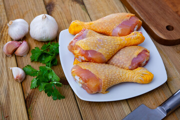 Fresh raw chicken leg drumsticks with greens and spices prepared for cooking on wooden background