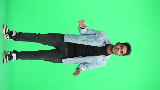 A man in a blue shirt on a green background in full height spreads his hands questioningly
