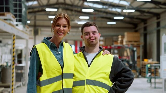 Young man with Down syndrome working in warehouse, colleague talking with him. Concept of workers with disabilities, support in workplace.