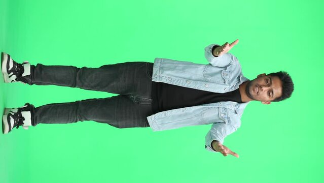 A man in a blue denim jacket on a green background throws his arms forward questioningly