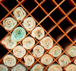 Closeup of a group of white folded towels with one green in a diamond shaped wooden rack at a spa or resort
