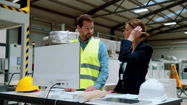 Female engineer reading technical documentation with project manager in modern industrial factory, talking about new production project, investment. Team management in manufacturing facility.