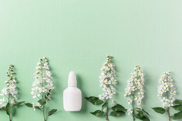 Seasonal spring allergies, fresh spring blooming branches tree and mock up white nasal spray bottle on green background, top view, minimal flat lay style. Seasonal allergy treatment concept.