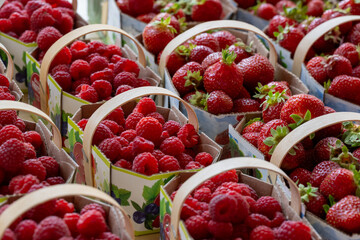 Baskets of fresh sweet organic red strawberries and raspberries for sale at a supermarket. The ripe berries are stored in cardboard baskets with wooden handles. The harvest is from a U-pick farm.