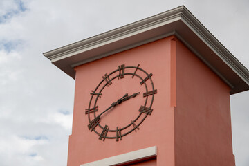 An exterior analog clock on a rose colored tower building with a cream color flat roof. The hands...