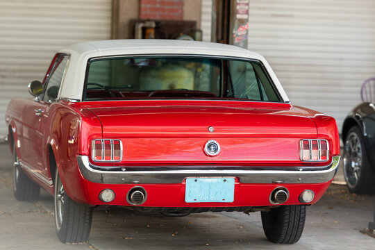 A vibrant candy apple red colored muscle car, the 1965 Ford Mustang, is parked in a garage. The vehicle has a white soft top.  The license plate indicates it's an antique convertible collectible.