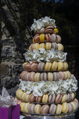 A pyramid or tier tower of an assortment of pastel colored French macaroons for a wedding. The pattern of traditional cream filled macarons is divided by a layer of white flowers on a vintage tray.  