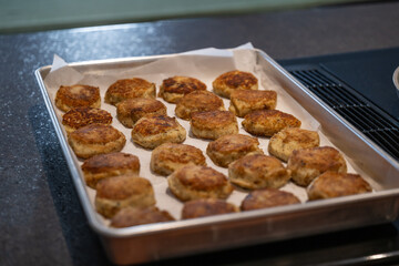A tray of cooked round salt cod fishcakes prepared on a barbeque. The savory, potato, salt codfish, and butter mixture are shaped into small patties and fried in butter until golden brown.