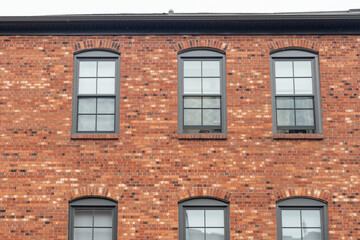 The exterior of an old red brick building with six glass double hung windows. The trim around the...