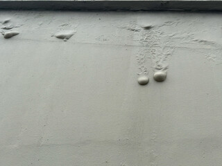 An exterior grey cement wall painted with a texture. Several bubbles or moisture blisters are...