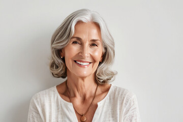 Portrait of beautiful older woman smiling and standing by white wall. A place for text, a banner for advertising. - obrazy, fototapety, plakaty