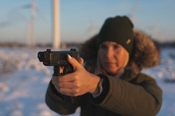 Obraz premium A girl takes aim with a 9mm pistol outdoors in winter. Soft focus photo.