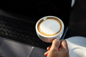 Business women hand holding white latte coffee cup and laptop on black table background.Hot coffee...