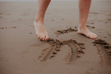 Drawing on the sand with your feet. 
Women's legs. Exercise against flat feet. Foot health.Clean sand. Inscriptions on the sand
