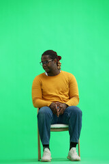 a man in a yellow sweater on a green background sits on a chair and looks to the side