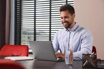 Happy young man working on laptop at table in office
