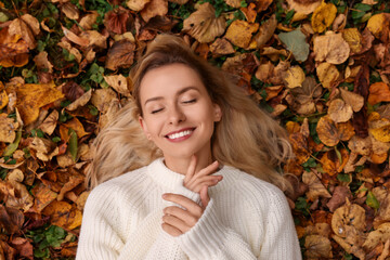 Smiling woman lying among autumn leaves outdoors, top view