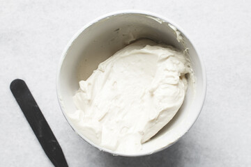 Top view of cream buttercream in a white mixing bowl, silky smooth american buttercream in a ceramic bowl, overhead view of smooth buttercream