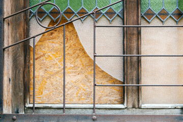 Broken vintage window with iron grilles in the street of Europe. Boarded up window after a break in. The tooth of time or the reflection of war - obrazy, fototapety, plakaty