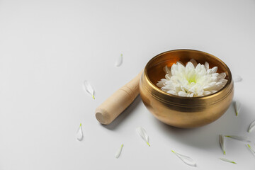 Tibetan singing bowl with water, beautiful chrysanthemum flower and mallet on white background, space for text