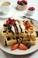 Delicious Belgian waffles with ice cream, berries and chocolate sauce served on white table, closeup