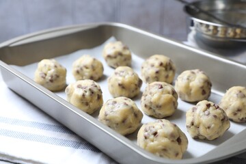 Baking pan with raw chocolate chip cookie balls on table, closeup