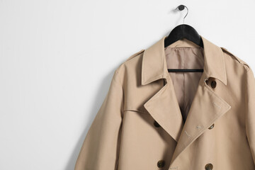 Hanger with beige trench coat on white wall, space for text