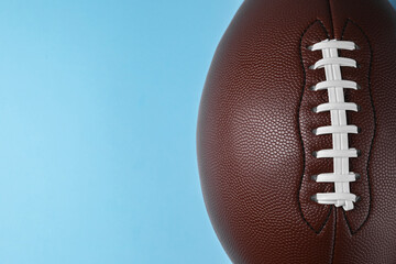 American football ball on light blue background, top view. Space for text