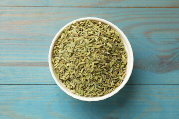 Fototapeta na wymiar Fennel seeds in bowl on light blue wooden table, top view
