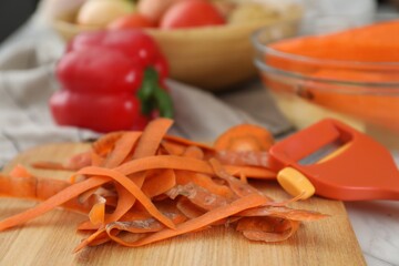 Wooden board with carrot peels and peeler on white table, closeup