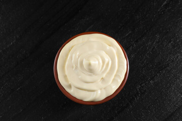 Fresh mayonnaise sauce in bowl on black table, top view
