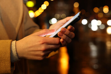 Woman using smartphone on night city street, closeup