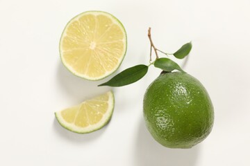 Fresh limes and green leaves on white background, flat lay