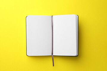 Open notebook with blank pages on yellow background, top view. Space for text