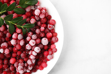 Frozen red cranberries and green leaves on white table, top view. Space for text