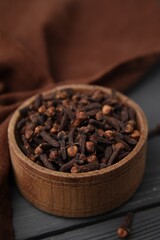 Aromatic cloves in bowl on grey wooden table, closeup
