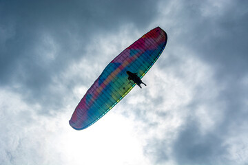 A person paragliding in the sky with a colorful parachute and safety harness.Mountains, Extreme sports in a cloudy day 