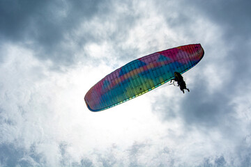 A person paragliding in the sky with a colorful parachute and safety harness.Mountains, Extreme sports in a cloudy day 
