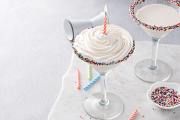 Birthday cake martini cocktail topped with whipped cream and a candle