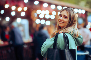 Happy Woman Holding a Shopping Bag at a Festive Fair. Cheerful millennial girl getting a bargain in a street market 
 - obrazy, fototapety, plakaty