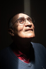 Old man or elder model with glasses with his face illuminated in the dark, black background. Caucasian or latino wearing blue clothes
