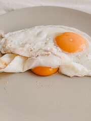 Vertical image of two fried eggs overlap and hidden under each other served on a dish.