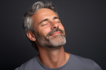 Obraz premium Studio portrait of handsome mature man with eyes closed, charcoal colored background.