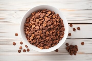 Top-down view of sweet chocolate cereal flakes in a bowl on a white wooden background.